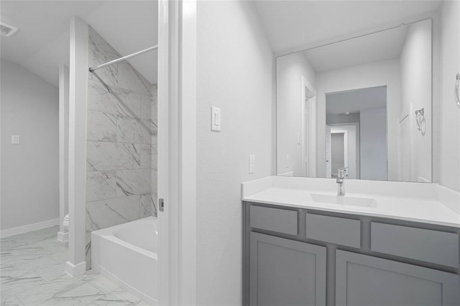 Secondary bath features tile flooring, bath/shower combo with tile surround, stained wood cabinets, beautiful light countertops, mirror, sleek fixtures and modern finishes.