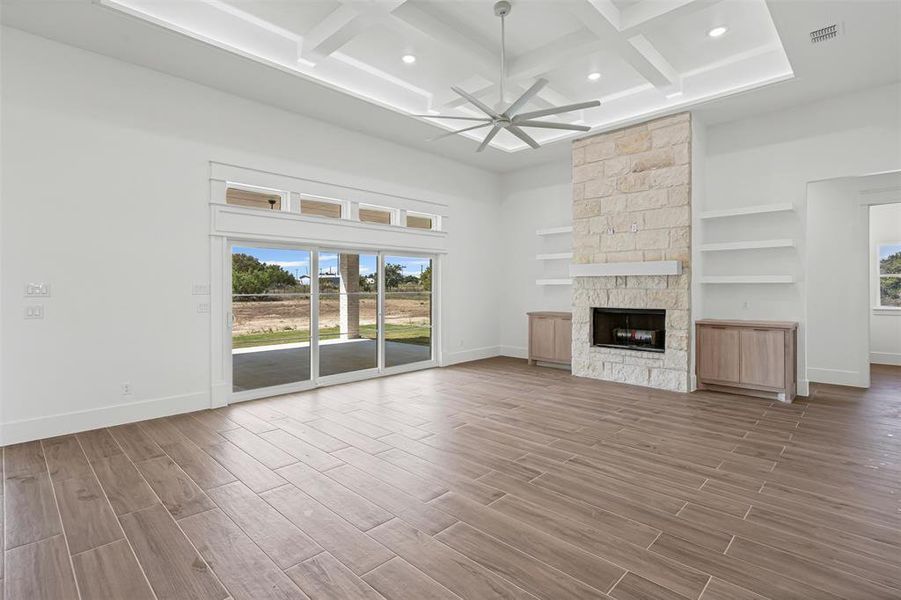 Unfurnished living room featuring light wood-style floors, a ceiling fan, a stone fireplace, a high ceiling, and coffered ceiling Unfurnished living room featuring light wood-style floors, a ceiling fan, a stone fireplace, a high ceiling, and coffered ceiling