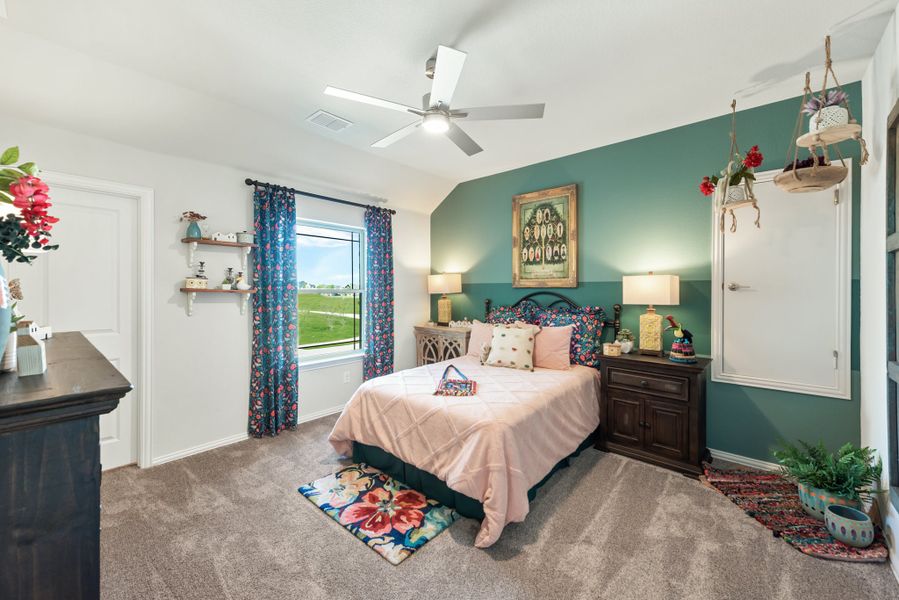 Bedroom with teal accent wall, ceiling fan, vaulted ceiling, and carpet flooring with colorful decor and window