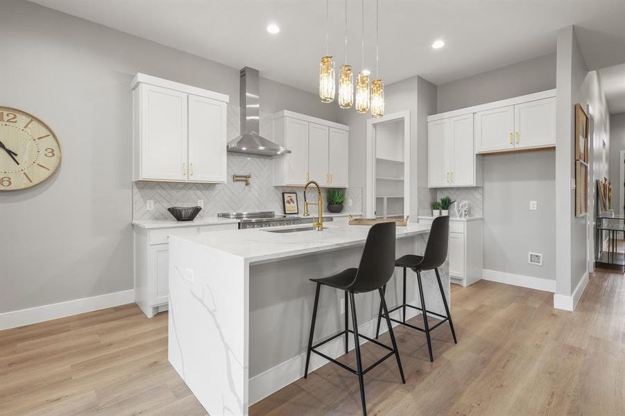 Kitchen featuring wall chimney exhaust hood, sink, an island with sink, and white cabinets