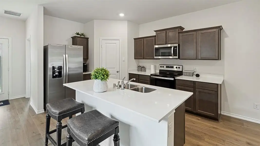 Kitchen with stainless steel appliances, a kitchen breakfast bar, dark wood finish cabinetry, a kitchen island with sink, and light wood-type flooring Kitchen with stainless steel appliances, a kitchen breakfast bar, dark wood finish cabinetry, a kitchen island with sink, and light wood-type flooring