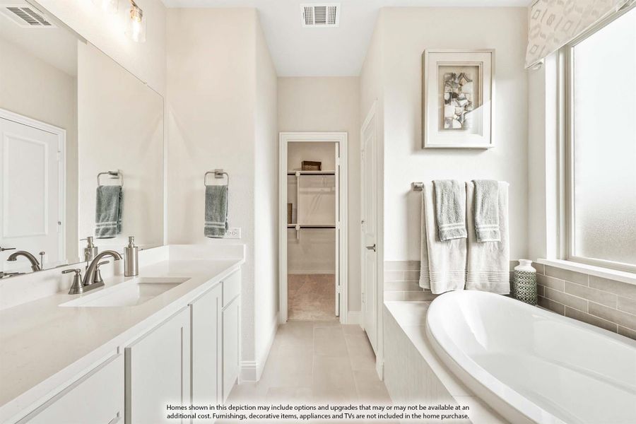 Master bathroom with white double vanity, soaking tub, and walk-in closet entry