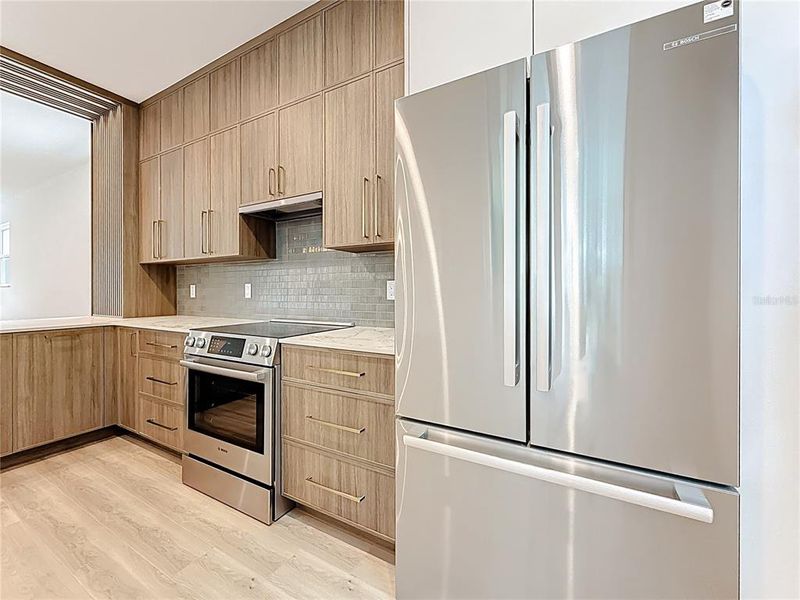 Sleek and modern kitchen featuring custom wood cabinetry, quartz waterfall countertops, stainless steel appliances, and stylish accent details — all bathed in natural light. Sleek and modern kitchen featuring custom wood cabinetry, quartz waterfall countertops, stainless steel appliances, and stylish accent details — all bathed in natural light.