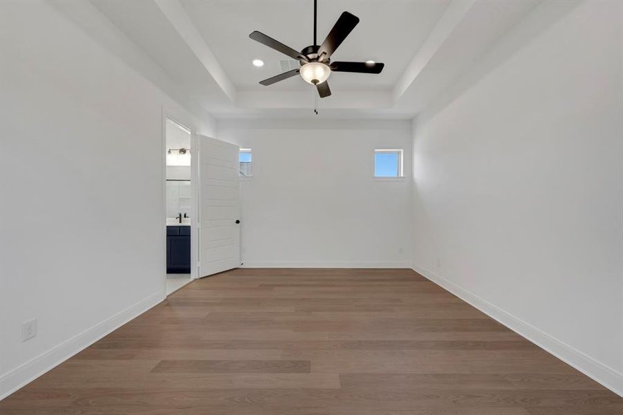 Empty room featuring a ceiling fan, dark wood-type flooring, a raised ceiling, and recessed lighting