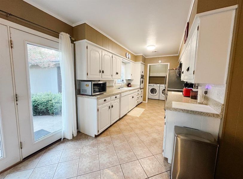 Kitchen with white cabinets, separate washer and dryer, ornamental molding, appliances with stainless steel finishes, and light tile patterned floors