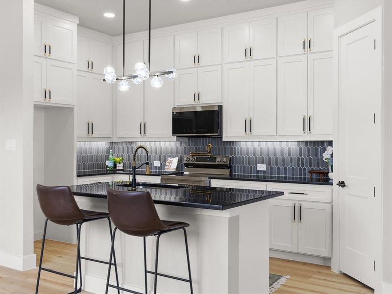 Modern kitchen featuring white shaker cabinetry, dark countertops, a unique picket tile backsplash, stainless steel appliances, and wood-finish flooring Modern kitchen featuring white shaker cabinetry, dark countertops, a unique picket tile backsplash, stainless steel appliances, and wood-finish flooring