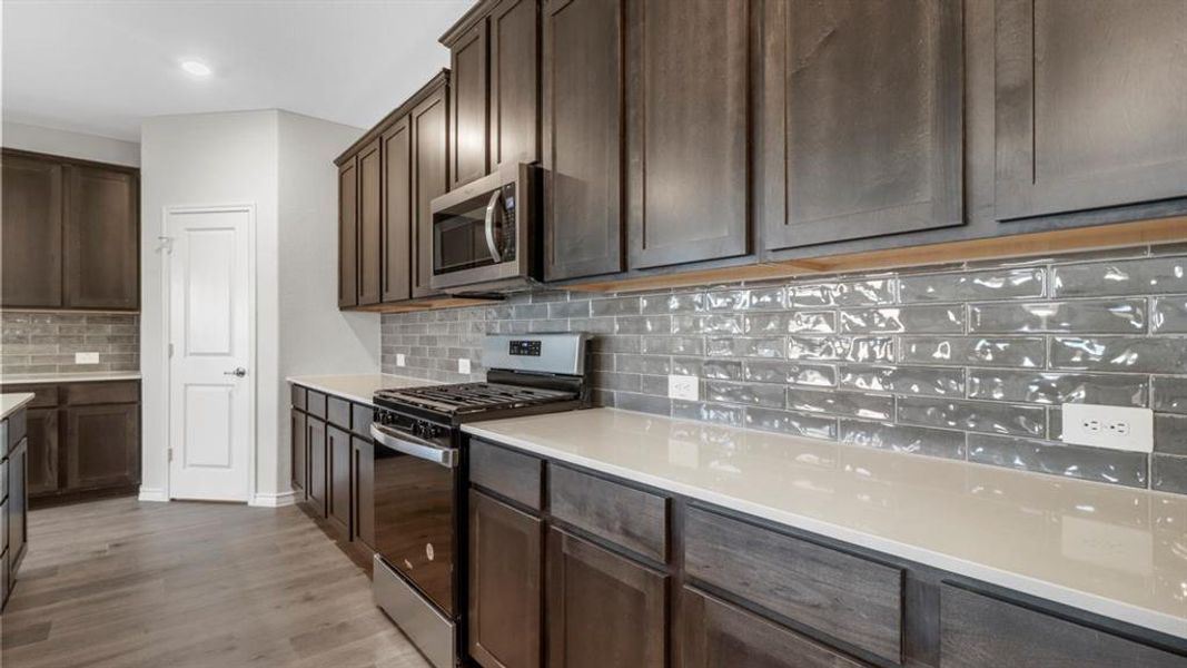 Kitchen featuring dark wood-finish cabinetry, light-toned countertops, and a subway tile backsplash
