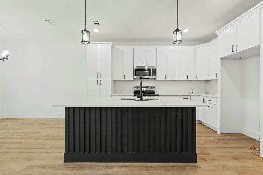 Kitchen with pendant lighting, light wood-style floors, a center island with sink, stainless steel appliances, and two tone color scheme