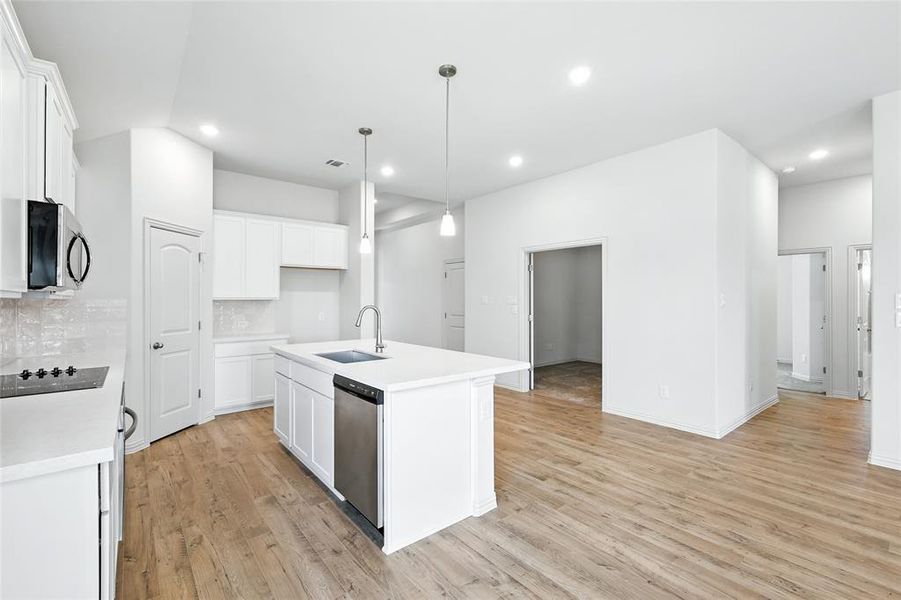 Kitchen with decorative backsplash, light wood-type flooring, hanging light fixtures, an island with sink, and white cabinets Kitchen with decorative backsplash, light wood-type flooring, hanging light fixtures, an island with sink, and white cabinets