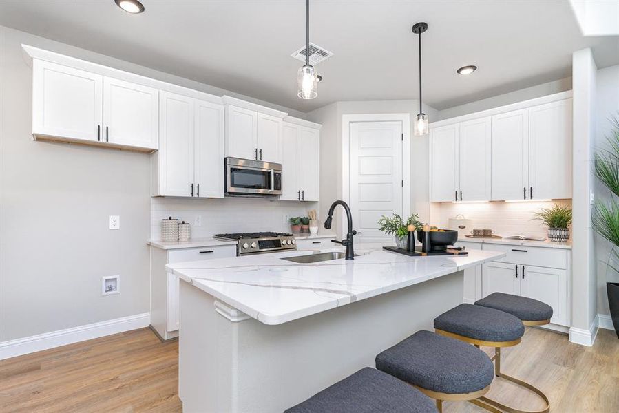 Kitchen featuring white cabinets, a center island with sink, sink, appliances with stainless steel finishes, and decorative light fixtures