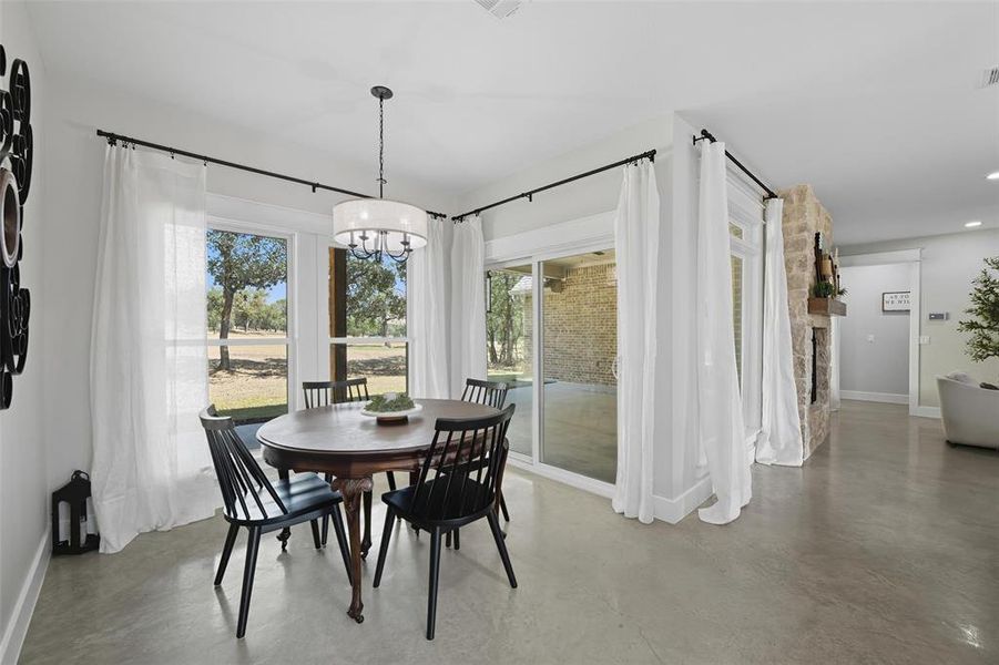Dining area featuring finished concrete flooring, a chandelier, and a stone fireplace Dining area featuring finished concrete flooring, a chandelier, and a stone fireplace