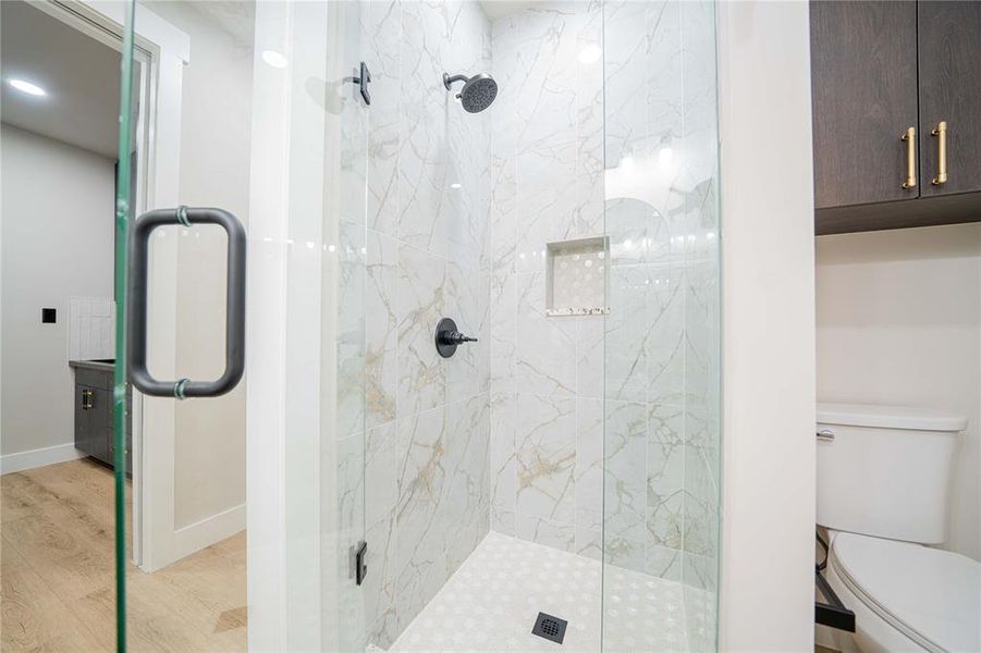 Glass-enclosed shower featuring large format tile walls, a built-in shower niche, and a contrasting dark shower system