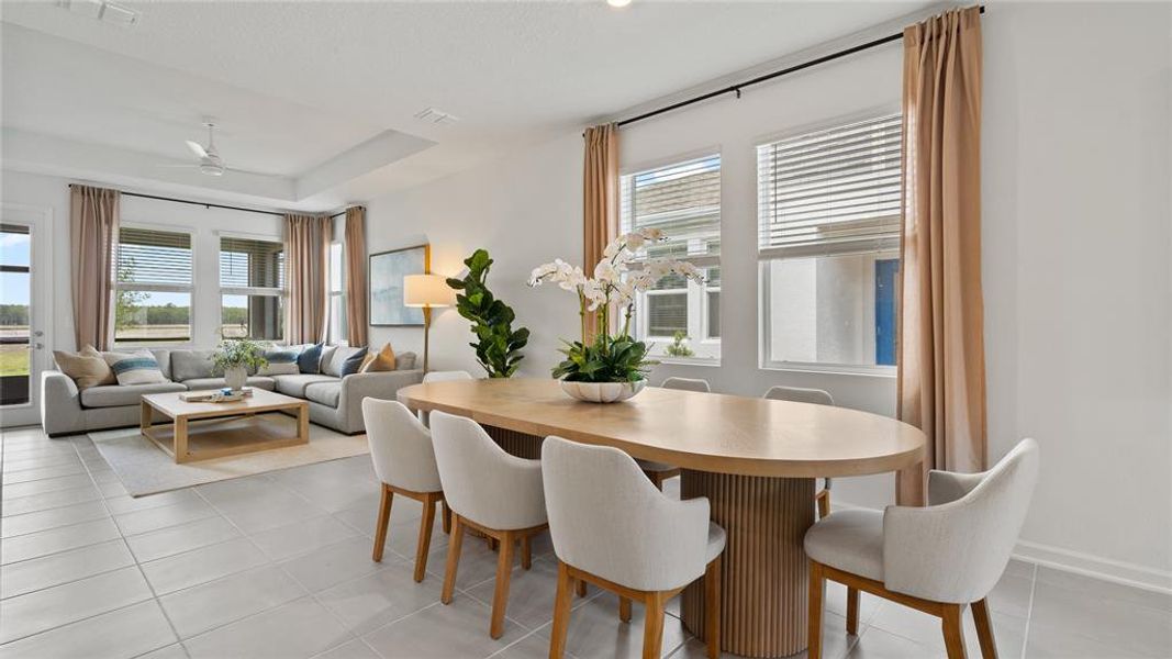 Dining area featuring healthy amount of natural light, light tile patterned flooring, a ceiling fan, and a raised ceiling Dining area featuring healthy amount of natural light, light tile patterned flooring, a ceiling fan, and a raised ceiling