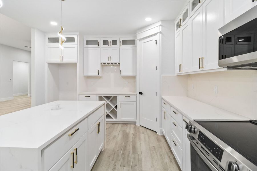 Kitchen featuring glass insert cabinets, appliances with stainless steel finishes, light wood-style flooring, white cabinets, and a center island