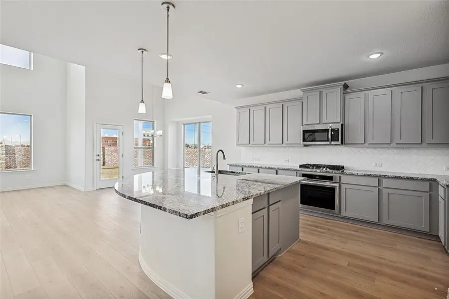 Kitchen featuring gray cabinetry, light stone counters, and backsplash Kitchen featuring gray cabinetry, light stone counters, and backsplash