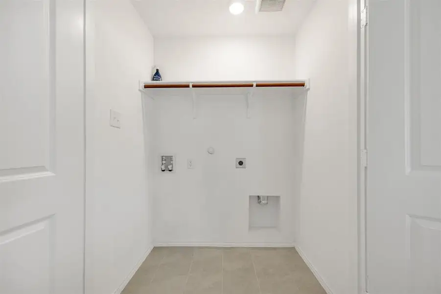 Dedicated utility area featuring a built-in shelf with hanging rod, light-toned tile flooring, and white walls