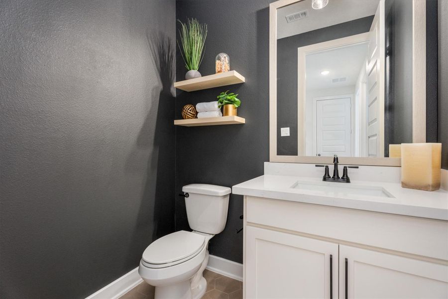 This modern bathroom features a sleek design with dark gray walls and a white vanity. It includes a toilet, a countertop sink, and a large mirror. Open shelves above the toilet provide space for decor and essentials, adding a touch of elegance.