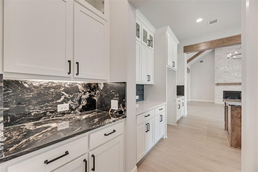 Kitchen with backsplash, glass insert cabinets, dark stone countertops, light wood-style flooring, and white cabinetry