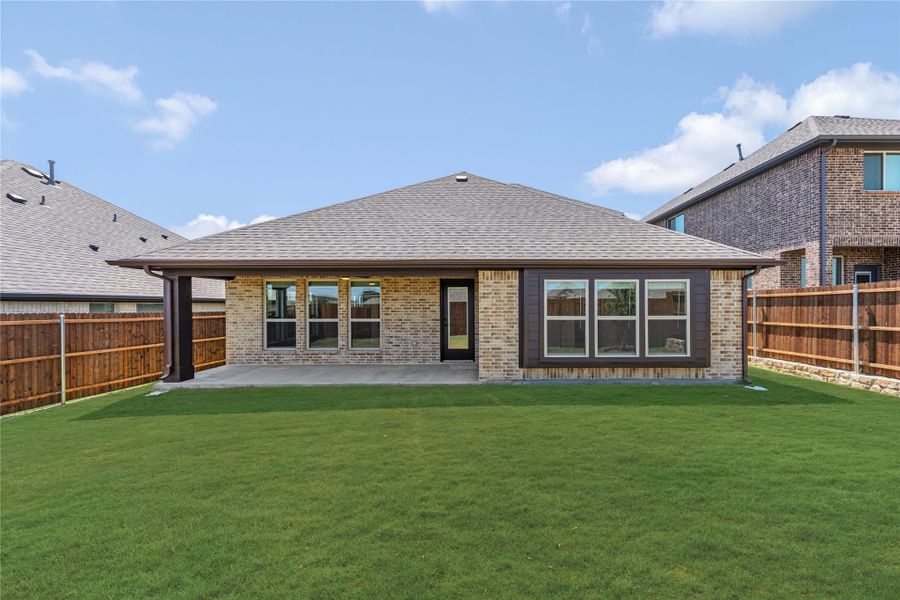 Rear exterior of brick home with covered patio, large windows, and fenced backyard with green lawn Rear exterior of brick home with covered patio, large windows, and fenced backyard with green lawn