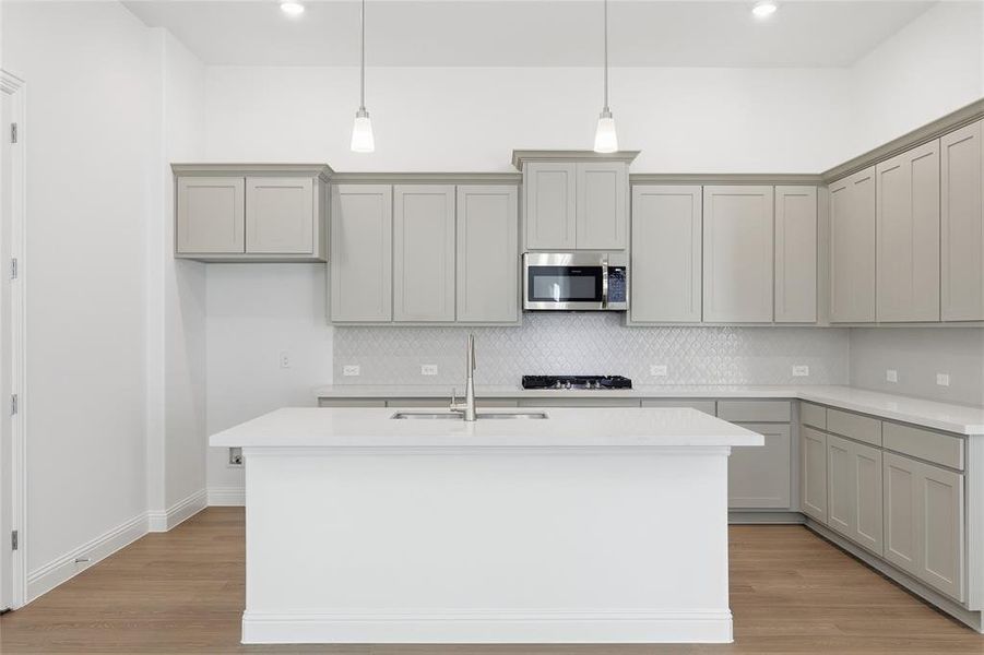 Kitchen with gray cabinetry, backsplash, light wood finished floors, stainless steel appliances, and light stone countertops