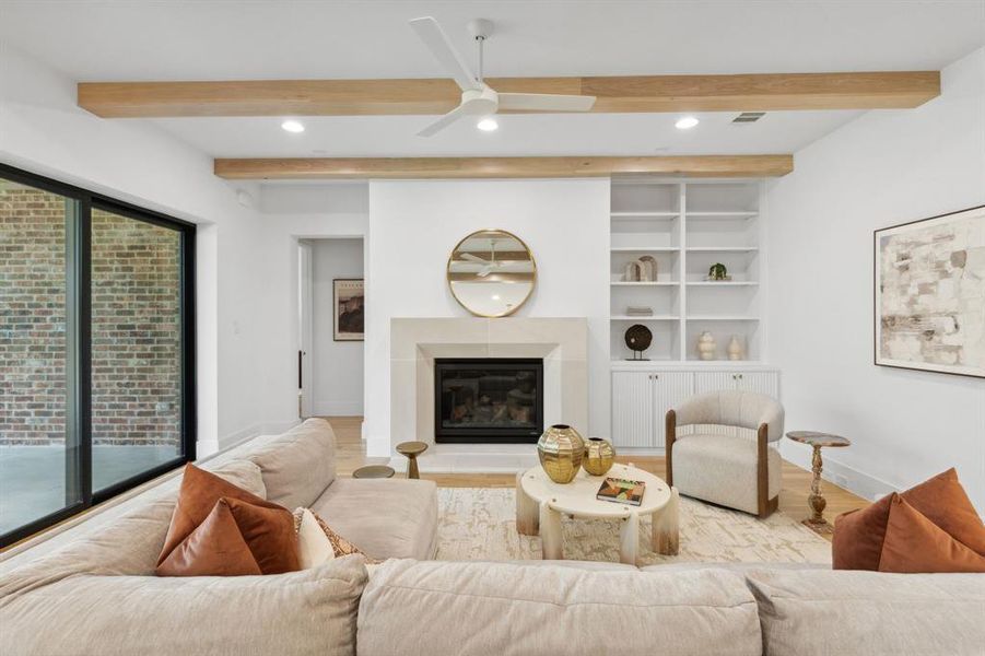 Living room with beam ceiling, ceiling fan, built in features, and light hardwood / wood-style flooring