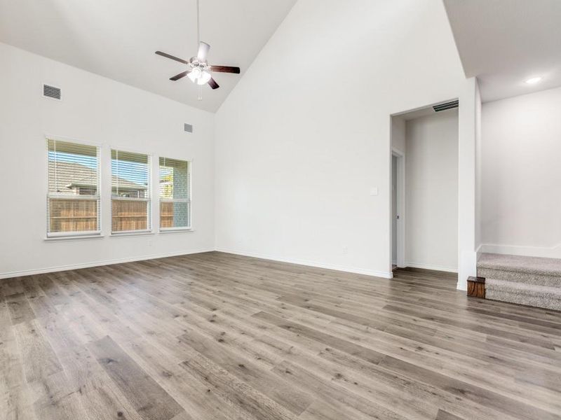 Unfurnished living room with high vaulted ceiling, light wood-style flooring, stairs, and a ceiling fan