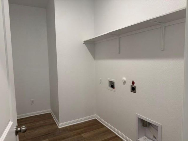 Dedicated utility space featuring wood-finish flooring, white walls, and a built-in storage shelf Dedicated utility space featuring wood-finish flooring, white walls, and a built-in storage shelf