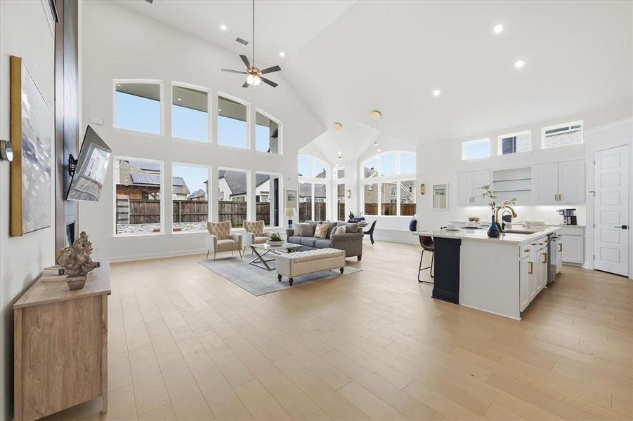 Open-concept living area featuring vaulted ceilings, a prominent kitchen island with seating, a full suite of kitchen cabinetry, wood-finish flooring, and multiple large windows