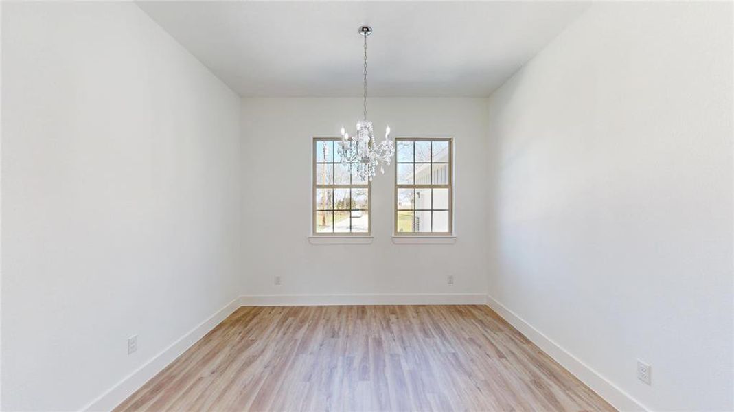 Spare room with light wood finished floors, baseboards, and a notable chandelier