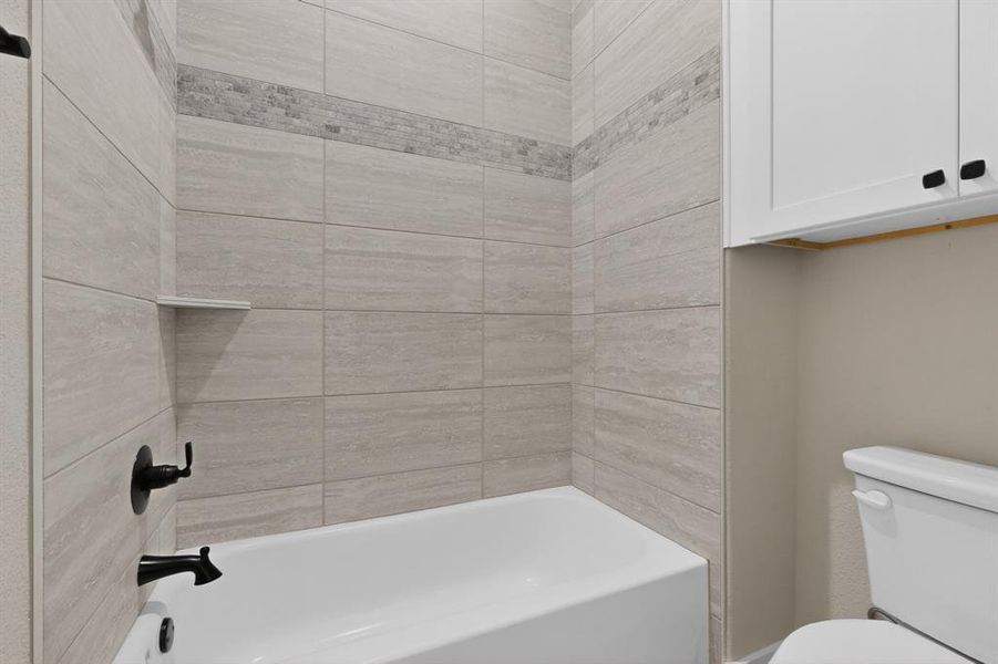 Bathtub with light-toned tiled surround, dark-finish fixtures, and a recessed shelf