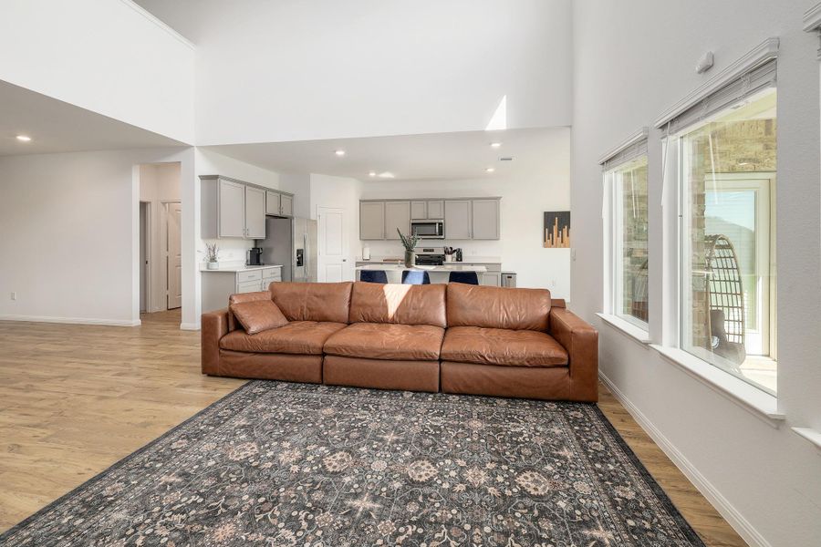 Expansive living area featuring vaulted ceilings, wood-finish flooring, and a kitchen visible in the background Expansive living area featuring vaulted ceilings, wood-finish flooring, and a kitchen visible in the background