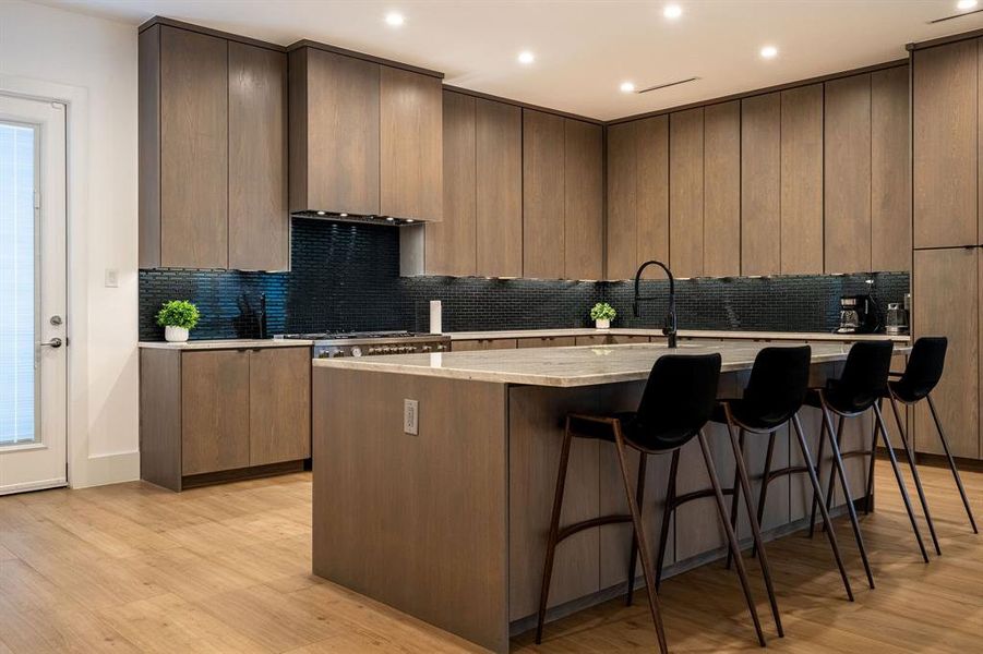 Kitchen featuring backsplash, light wood-type flooring, an island with sink, and a kitchen bar Kitchen featuring backsplash, light wood-type flooring, an island with sink, and a kitchen bar
