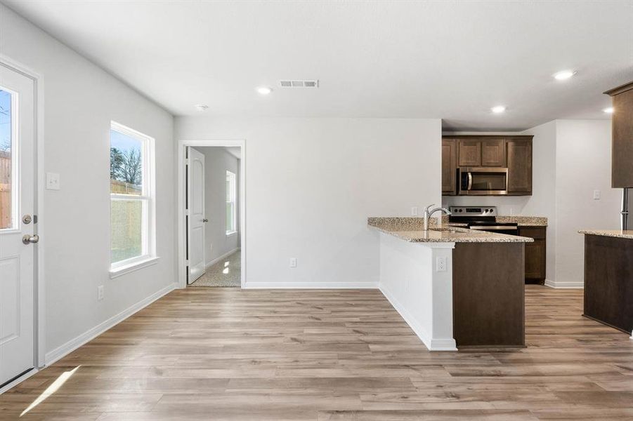 Kitchen with light stone counters, stainless steel appliances, sink, kitchen peninsula, and light hardwood / wood-style flooring