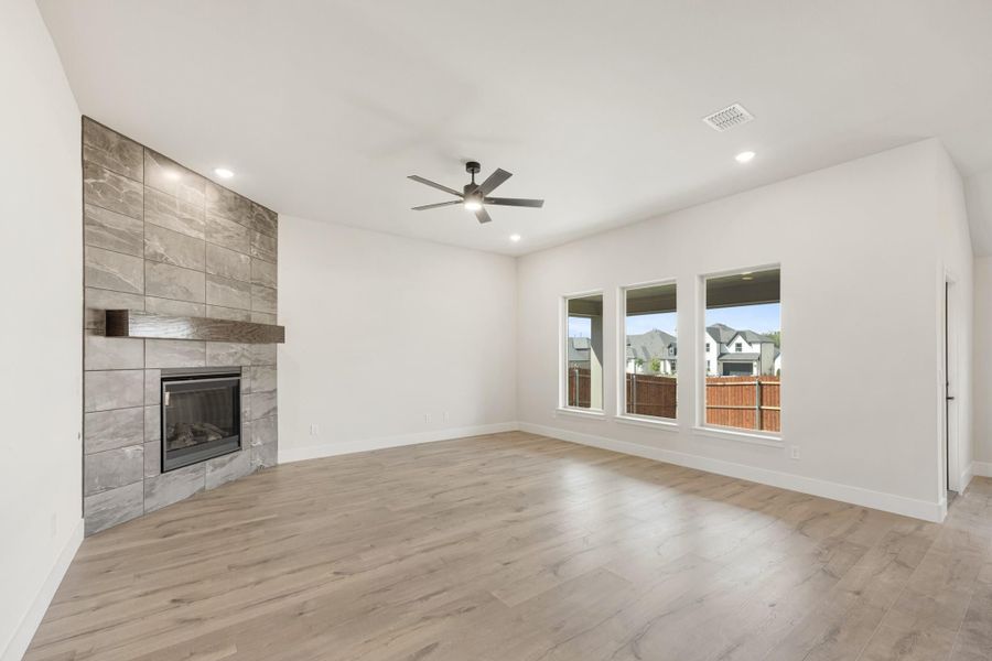 Open living room with floor-to-ceiling tile fireplace, light wood floors, and ceiling fan