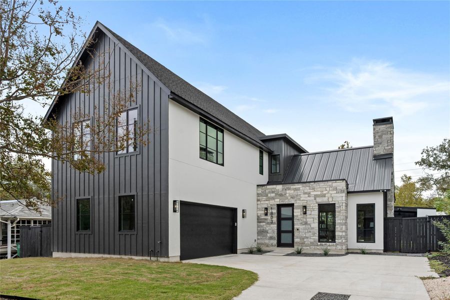View of front of property with board and batten siding, concrete driveway, an attached garage, stone siding, and a chimney
