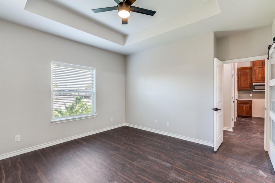Spare room featuring a tray ceiling, dark wood-style floors, and a barn door Spare room featuring a tray ceiling, dark wood-style floors, and a barn door