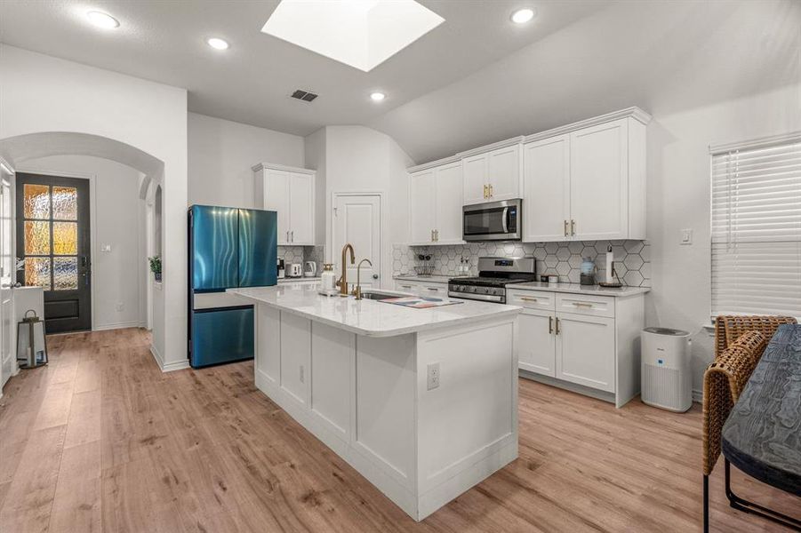 Kitchen with a center island with sink, vaulted ceiling with skylight, light hardwood / wood-style floors, white cabinetry, and stainless steel appliances