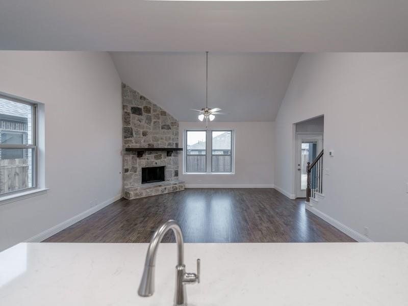 Unfurnished living room with lofted ceiling, dark hardwood / wood-style floors, a stone fireplace, and ceiling fan