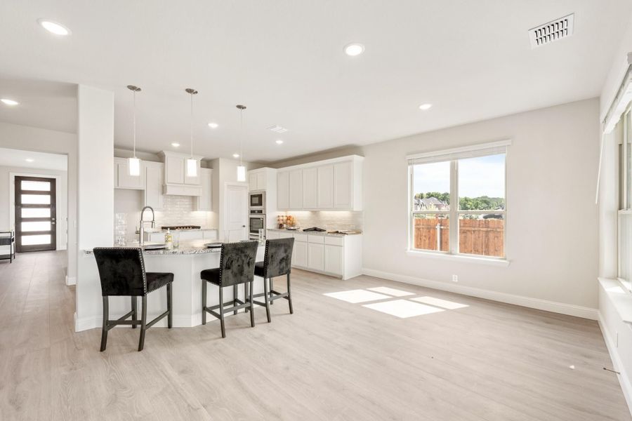 Open kitchen with white cabinets, granite island, pendant lights, and light hardwood floors