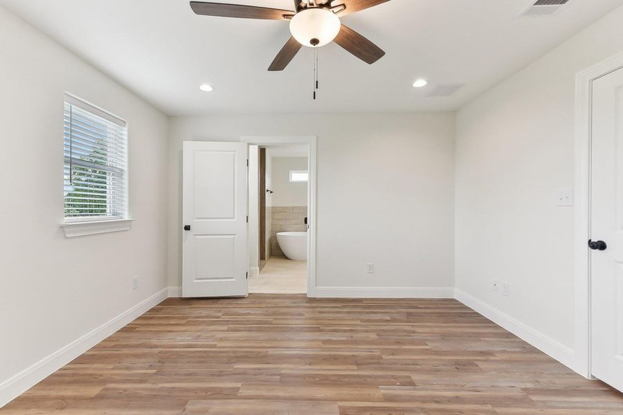 Primary bedroom with light wood-type flooring, visible vents, baseboards, recessed lighting, and ensuite bath