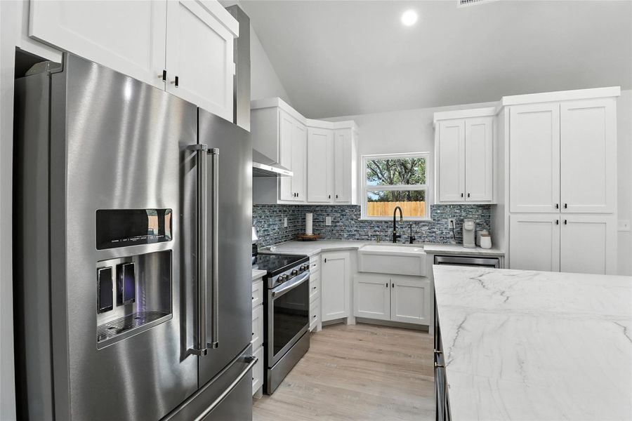 Kitchen with appliances with stainless steel finishes, light stone counters, white cabinets, tasteful backsplash, and light wood-style floors