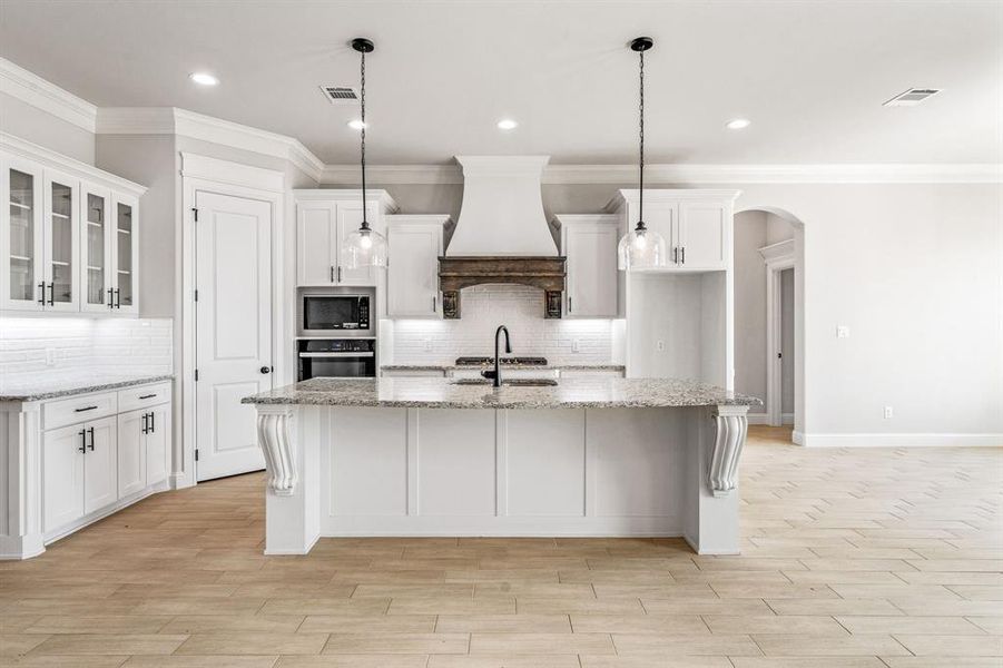 Kitchen featuring glass insert cabinets, ornamental molding, white cabinets, arched walkways, and tasteful backsplash