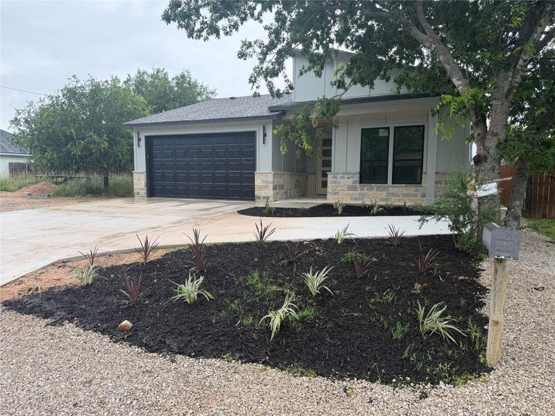 Modern home with an attached garage and stone accents welcomes you to a freshly landscaped yard.