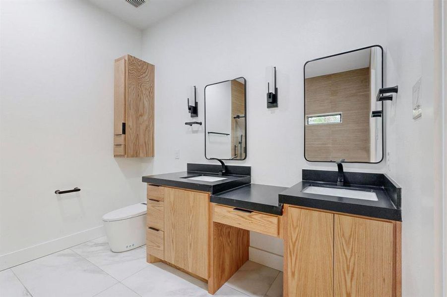Dual vanity with wood-finish cabinetry, dark countertops, and undermount sinks Dual vanity with wood-finish cabinetry, dark countertops, and undermount sinks