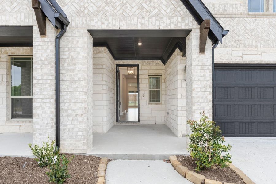 Covered front entry with light stone exterior, black door, dark wood ceiling, and adjacent garage door