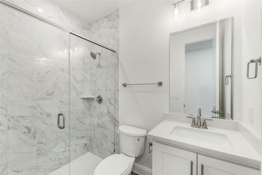 Bathroom with marble-tile walk-in shower, glass door, white vanity, and toilet