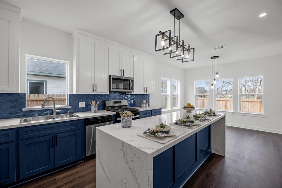 Striking blend of blue and white cabinetry, a sleek marble island, and stainless steel appliances. Natural light floods in through multiple windows, highlighting the elegant pendant lighting and spacious layout, perfect for entertaining. Striking blend of blue and white cabinetry, a sleek marble island, and stainless steel appliances. Natural light floods in through multiple windows, highlighting the elegant pendant lighting and spacious layout, perfect for entertaining.