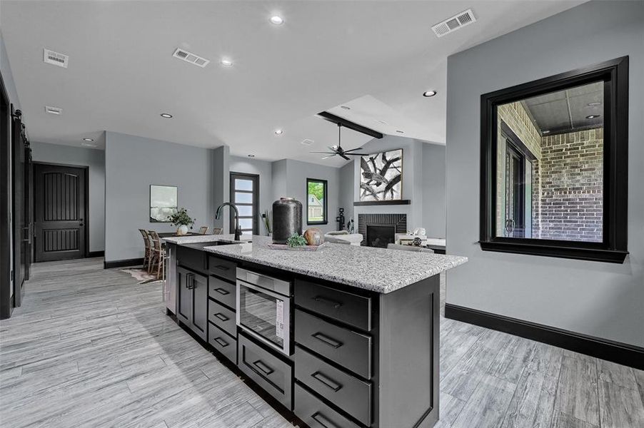 Kitchen featuring stainless steel microwave, a brick fireplace, light wood-type flooring, baseboards, and recessed lighting Kitchen featuring stainless steel microwave, a brick fireplace, light wood-type flooring, baseboards, and recessed lighting