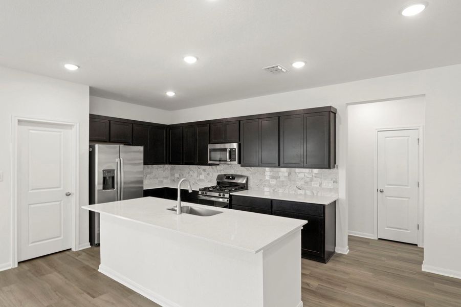 Kitchen featuring stainless steel appliances, light wood-style flooring, an island with sink, light stone countertops, and tasteful backsplash