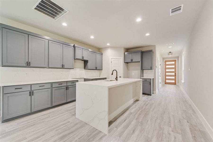 Kitchen with gray cabinetry, a center island with sink, light wood-type flooring, recessed lighting, and backsplash Kitchen with gray cabinetry, a center island with sink, light wood-type flooring, recessed lighting, and backsplash
